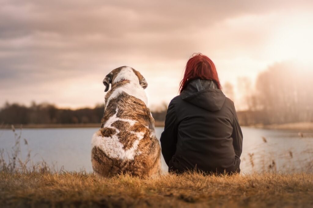 mergina sėdi su šuniu prie ežero