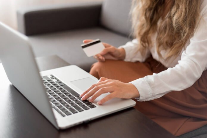 Moters atliekamas mokėjimas dalimis internetu – rankoje laikoma banko kortelė, pirkimas vyksta per nešiojamą kompiuterį