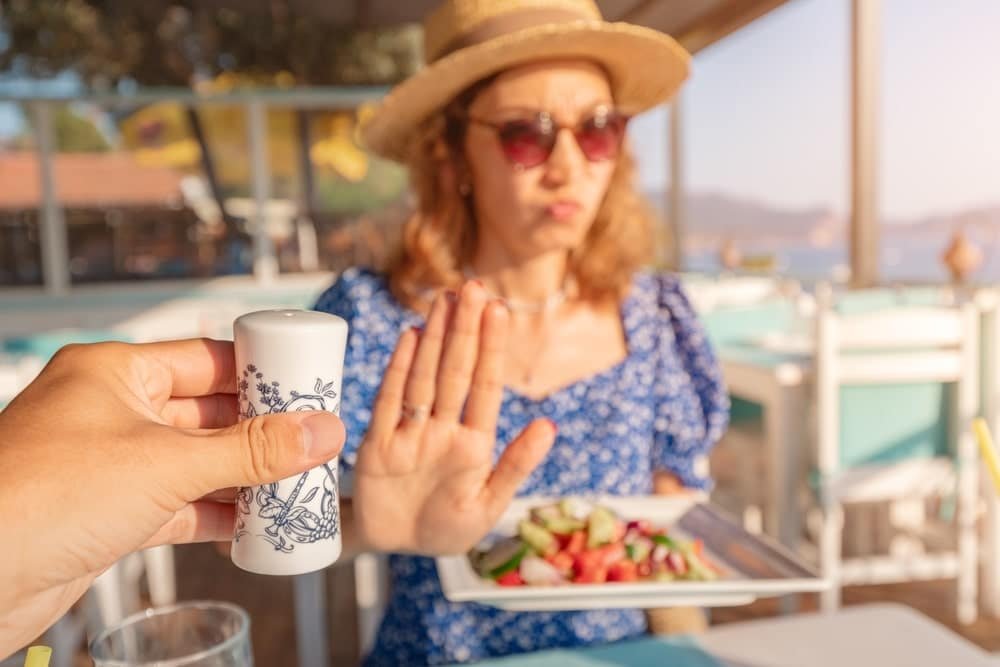 Moteris restorane mostu rankos atsisako papildomai sūdyti salotas, šalia laikomas druskos indelis.