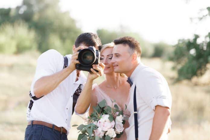 Fotografas kartu su jaunavedžiais peržiūri vestuvių nuotraukas – džiaugsmo ir tikrų emocijų įamžinimas.